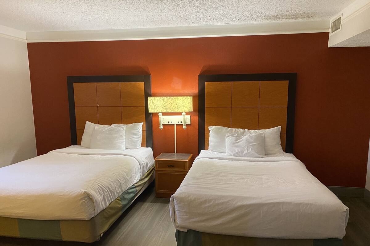 Une chambre d’hôtel avec deux lits, une table de chevet, une lampe et une tête de lit en bois.