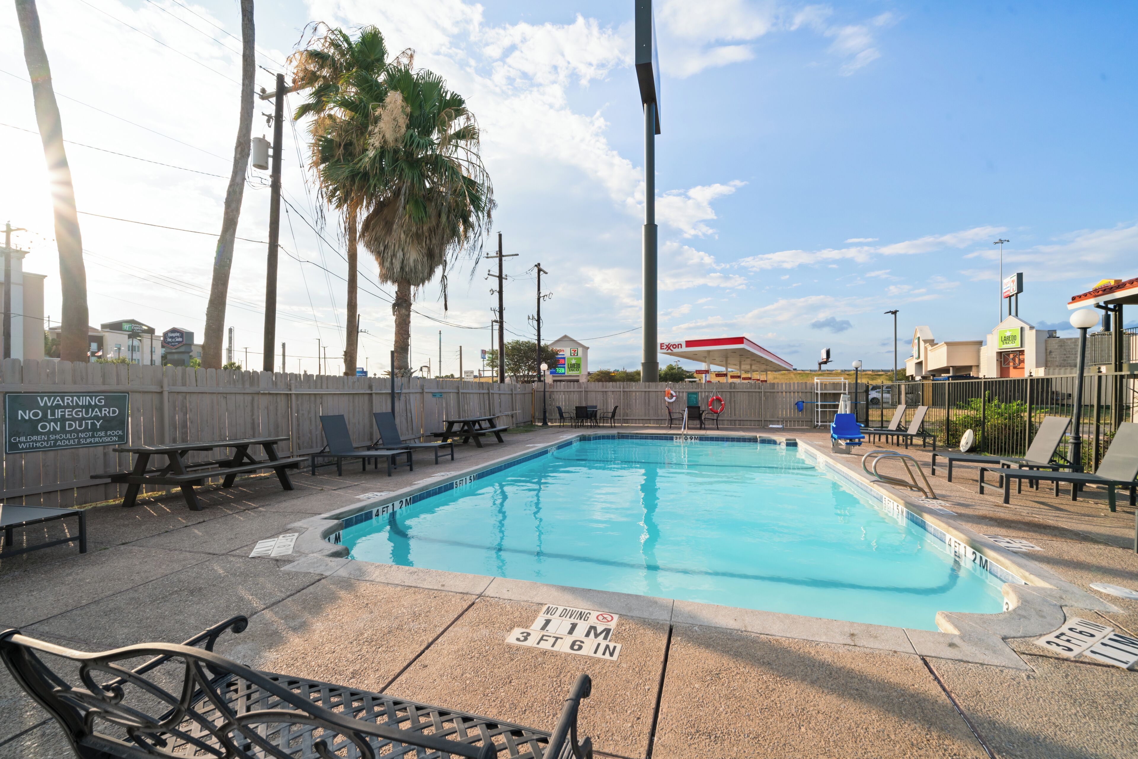 A swimming pool with a lifeguard warning sign, lounge chairs, and a picnic table.