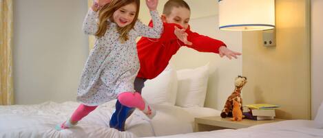A hotel room with a bed, a nightstand with a lamp, and a stuffed giraffe toy on the nightstand.