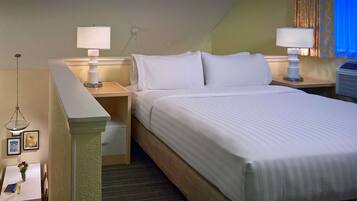 A hotel room with a neatly made bed, two bedside lamps, a small table with a vase of flowers, and a picture frame.