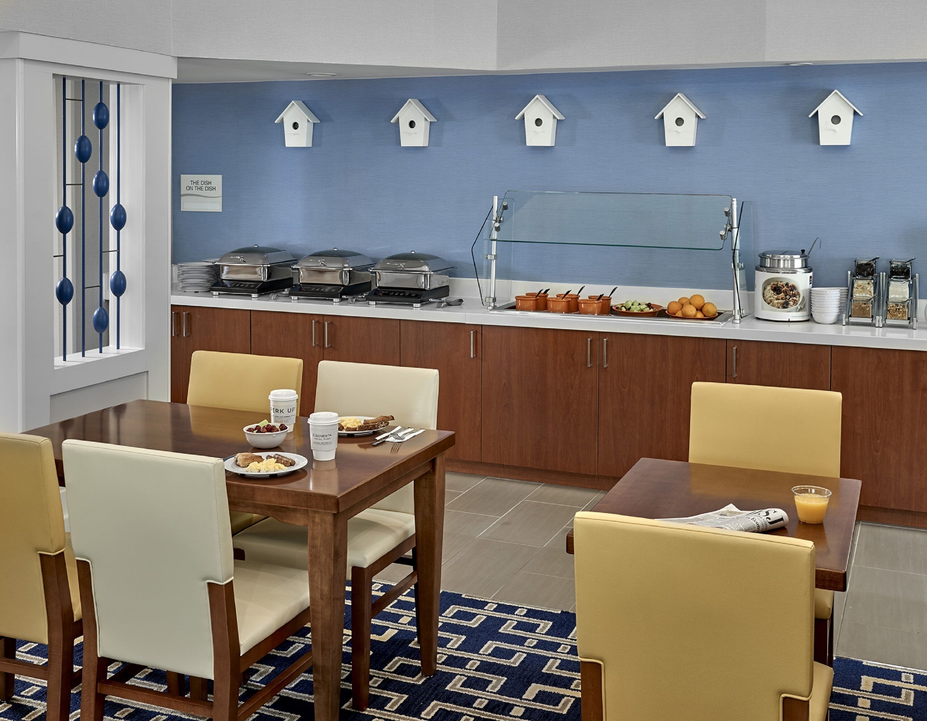 Een moderne keuken met een eetgedeelte, met een buffetopstelling, houten kastjes en een blauwe achterwand met decoraties van vogelhuisjes.