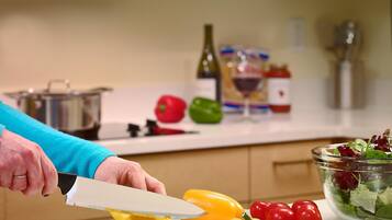 A kitchen counter with a person slicing a yellow bell pepper, a bowl of salad, and various kitchen items in the background.
