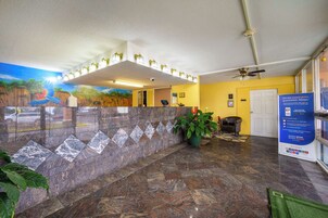 Un área de recepción con pared de mármol, un mural, ventilador de techo y un cartel.