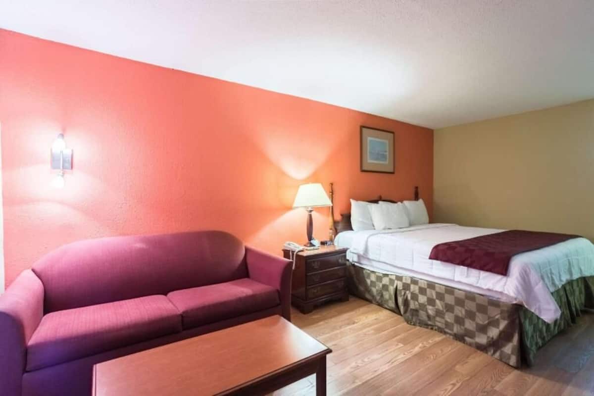 Una habitación de hotel con cama, sofá, mesita de noche y lámpara.