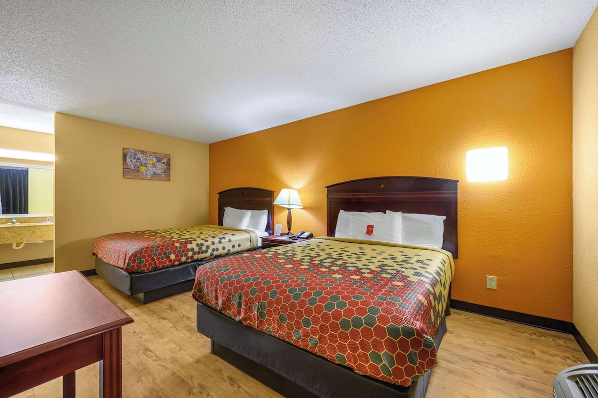 Habitación de hotel con dos camas, un escritorio, una lámpara y un cuadro en la pared.