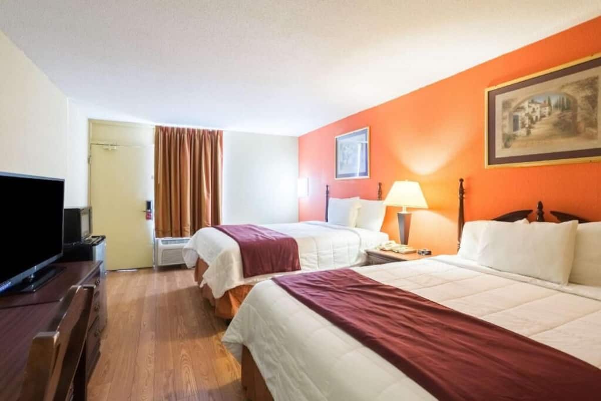 Una habitación de hotel con dos camas, televisión, lámpara y un cuadro en la pared.