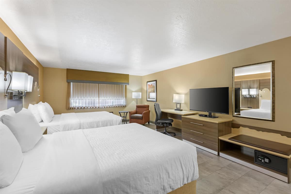 A hotel room with two beds, a desk with a TV, a chair, a desk lamp, and a safe.