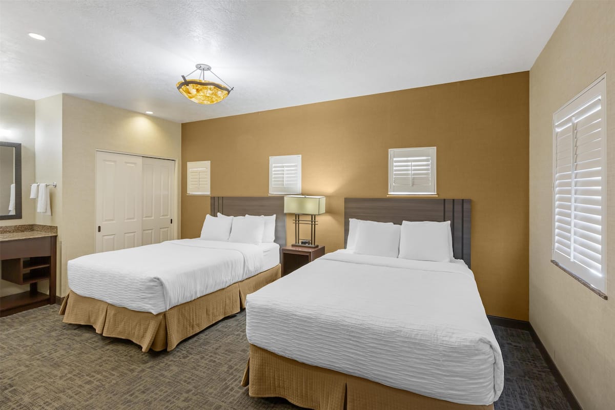 A hotel room with two beds, a bathroom, and a chandelier.