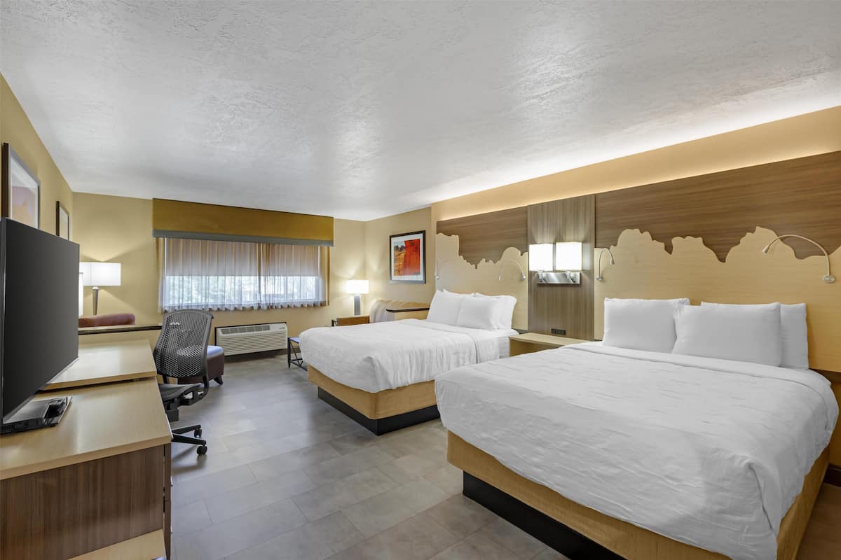 A hotel room with two beds, a desk, a TV, and a chair.