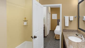 A bathroom with a bathtub, a sink, and a mirror. There is a towel rack with towels and a shelf with toiletries.