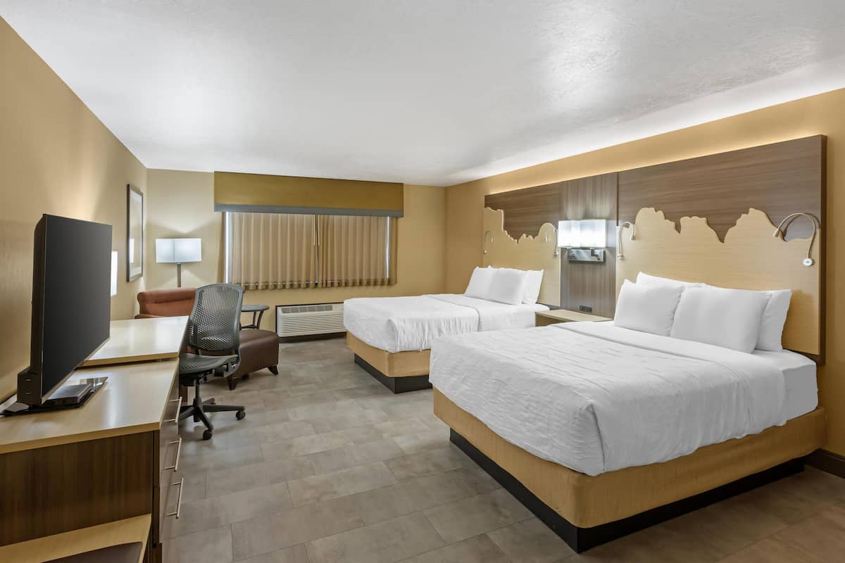 A hotel room with two beds, a desk with a computer, a chair, a TV, and a window with curtains.