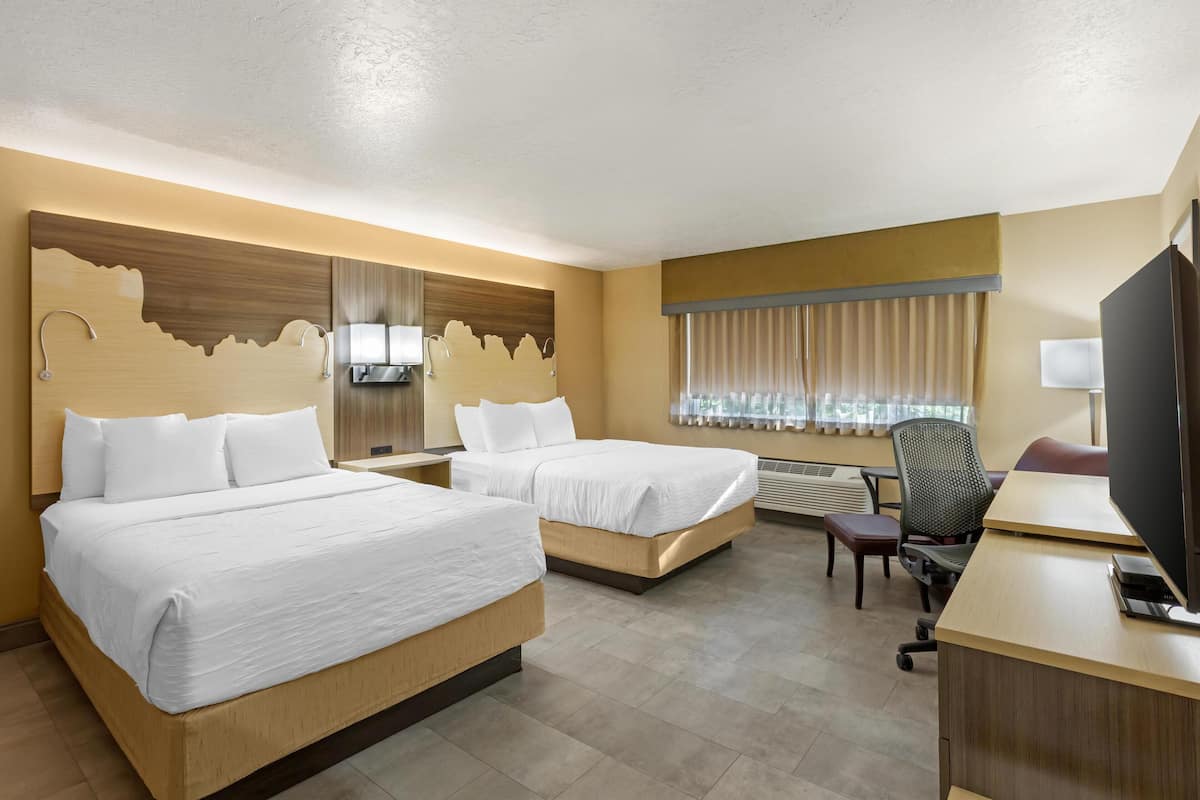 A hotel room with two beds, a desk, a chair, and a television.