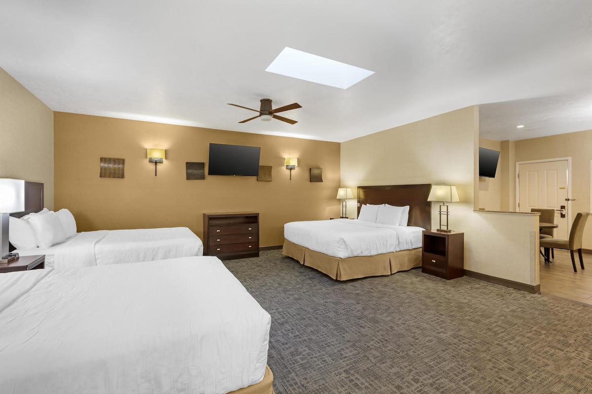 A hotel room with two beds, a ceiling fan, a flat-screen TV, wall-mounted lamps, a desk, and a mirror.