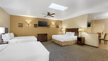 A hotel room with two beds, a ceiling fan, a flat-screen TV, wall-mounted lamps, a desk, and a mirror.