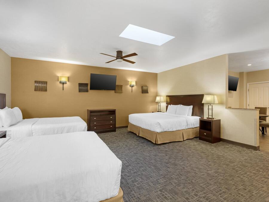 A hotel room with two beds, a ceiling fan, a flat-screen TV, wall-mounted lamps, a desk, and a mirror.