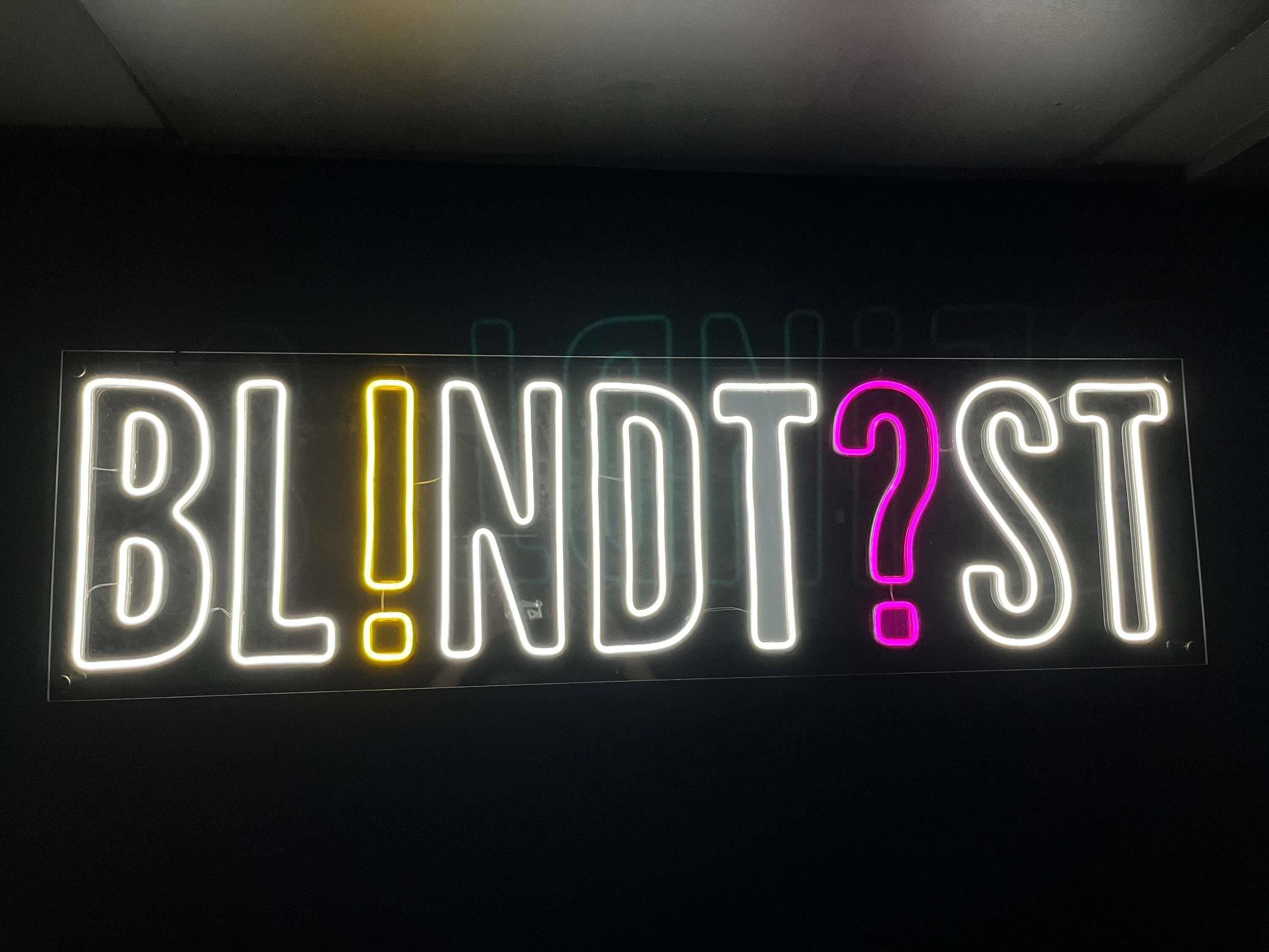 Um letreiro de neon com o texto 'BL!ND?ST' em branco, amarelo e rosa.