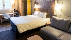 A hotel room with a bed, a desk, a chair, a sofa, and a wall-mounted lamp. - ibis Compiègne (Compiègne)
