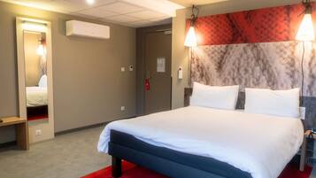 Habitación de hotel con cama, espejo, equipo de aire acondicionado, alfombra roja y puerta con detector de incendios.