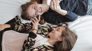 Dos personas acostadas sobre una cama con sábana blanca, una sosteniendo un teléfono inteligente.