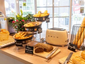 A bakery display with various breads and pastries, including croissants, pain au chocolat, and baguette, with a toaster and a knife on the counter.