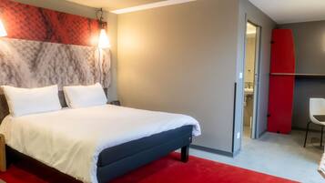 Una habitación de hotel moderna con una cama, una alfombra roja, un cabecero de mármol y una tabla de surf roja apoyada contra la pared.