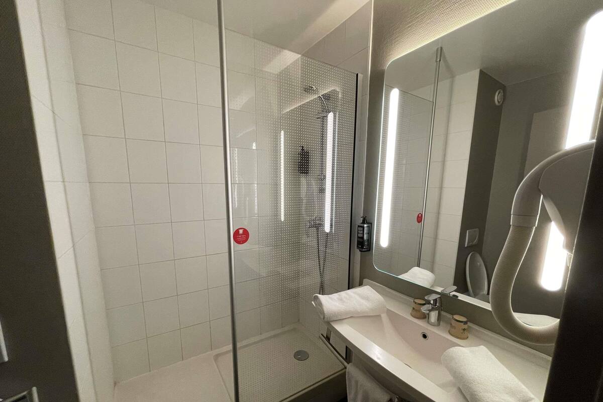 A modern bathroom with a glass-enclosed shower, a white sink, and a large mirror.