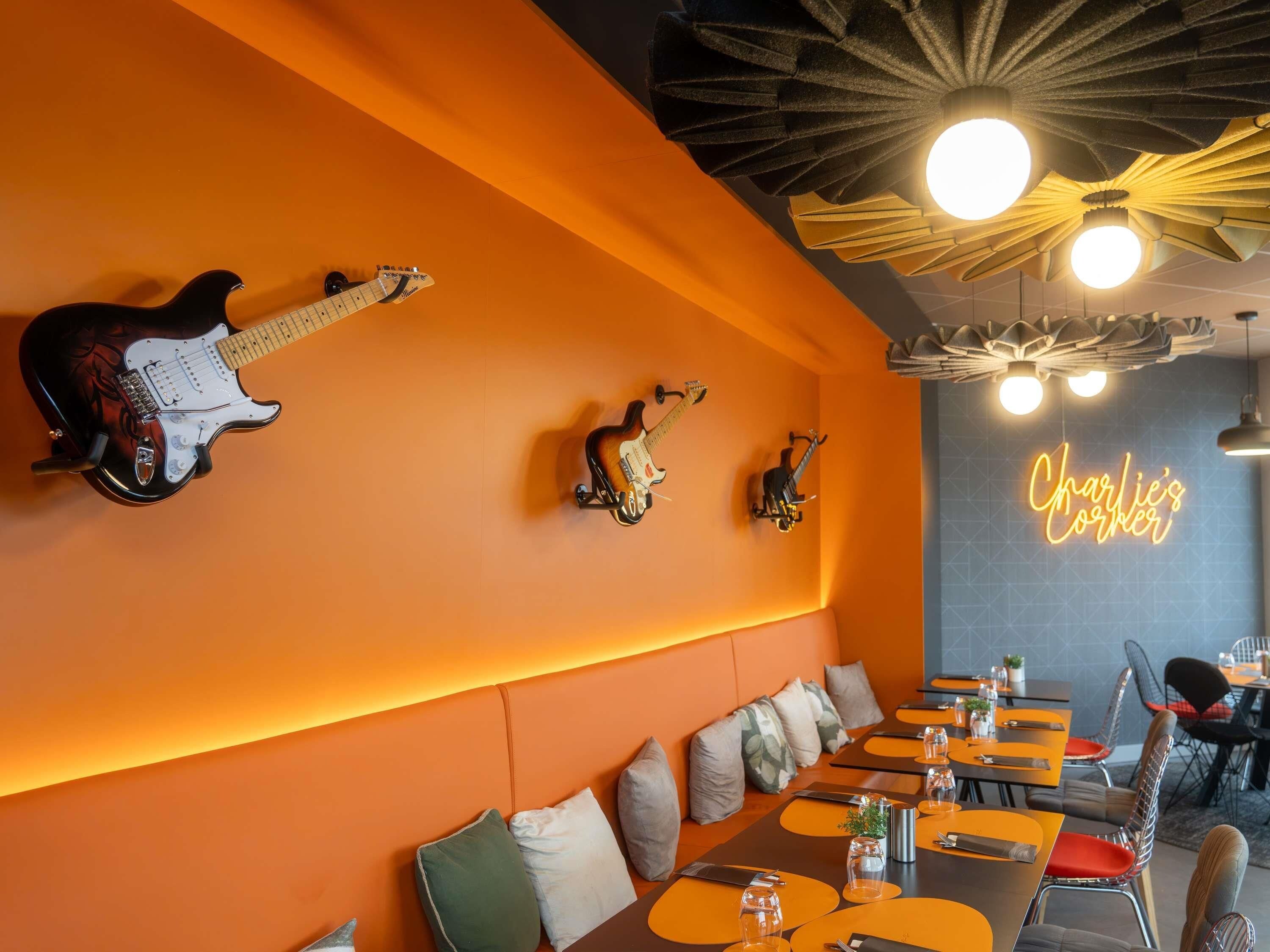 Un restaurante con paredes color naranja, varias guitarras expuestas y un letrero de neón que dice 'Charlie’s Corner'.
