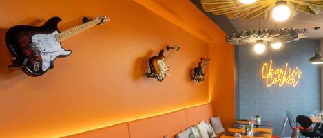 Un restaurante con paredes color naranja, varias guitarras expuestas y un letrero de neón que dice 'Charlie’s Corner'.