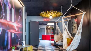 A modern interior with a geometric black and white floor pattern, a hammock chair, a small round table with a plant, and a large digital screen displaying abstract art. - ibis Compiègne (Compiègne)