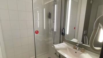 A modern bathroom with a glass shower enclosure, a white sink with a mirror, and a handheld showerhead.