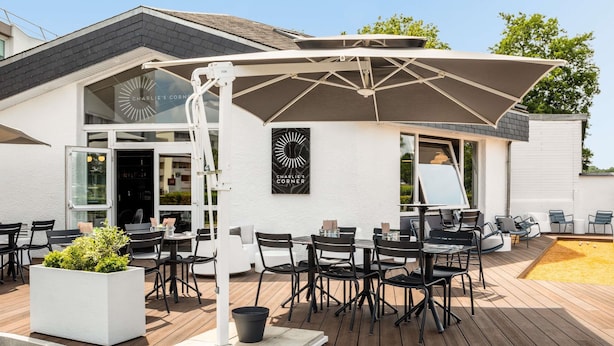 An outdoor seating area with tables and chairs, a large umbrella, and a sign reading "CHARLIE'S CORNER". - ibis Compiègne (Compiègne)