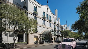 Un hotel moderno con fachada clásica, un acceso cubierto y un taxi rosa estacionado frente a él.