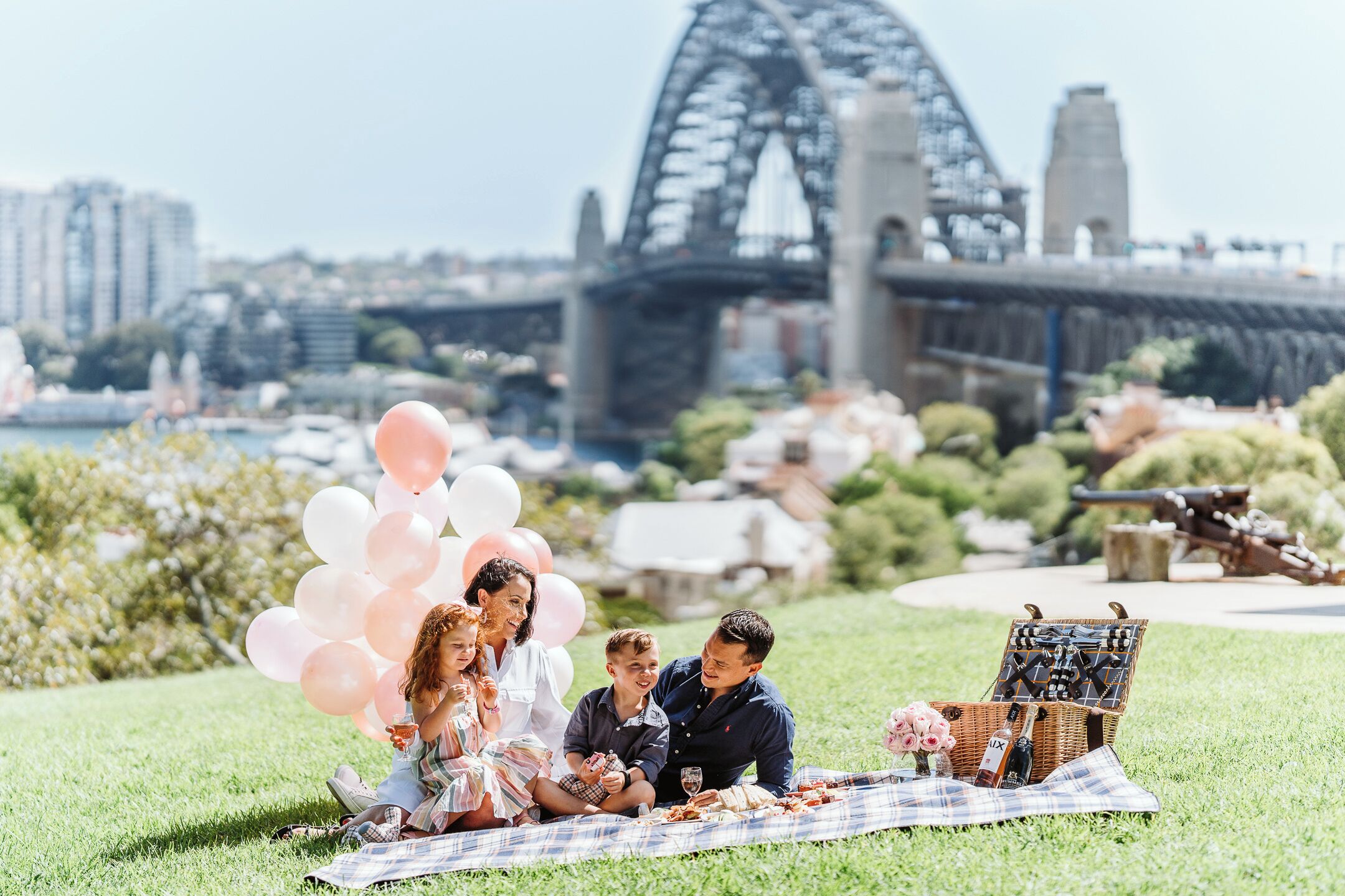 Un montaje para picnic con cesto, mesa, globos y una vista panorámica de un puente y el paisaje urbano.