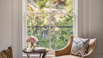 Une pièce avec une grande fenêtre, un lit, une chaise et une petite table sur laquelle est posé un vase de fleurs.