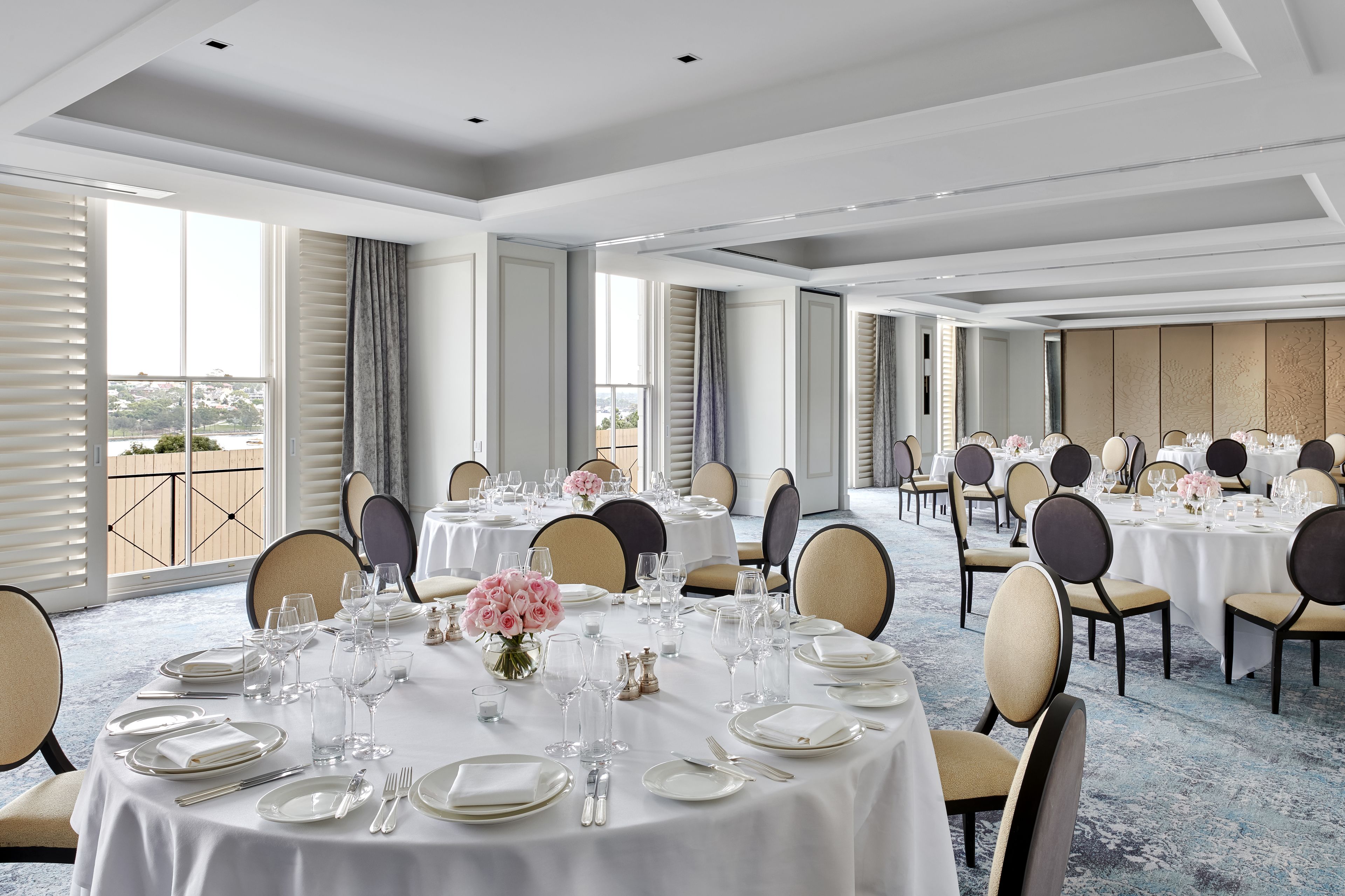A large banquet hall with round tables set for dining, featuring white tablecloths and floral centerpieces.