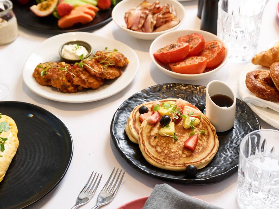 Un bufé de desayuno con diversos platos, incluyendo panqueques, fruta y pastelería.
