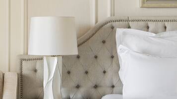 A neatly made bed with white linens, a tufted headboard, a bedside table with a lamp, and a framed picture on the wall.