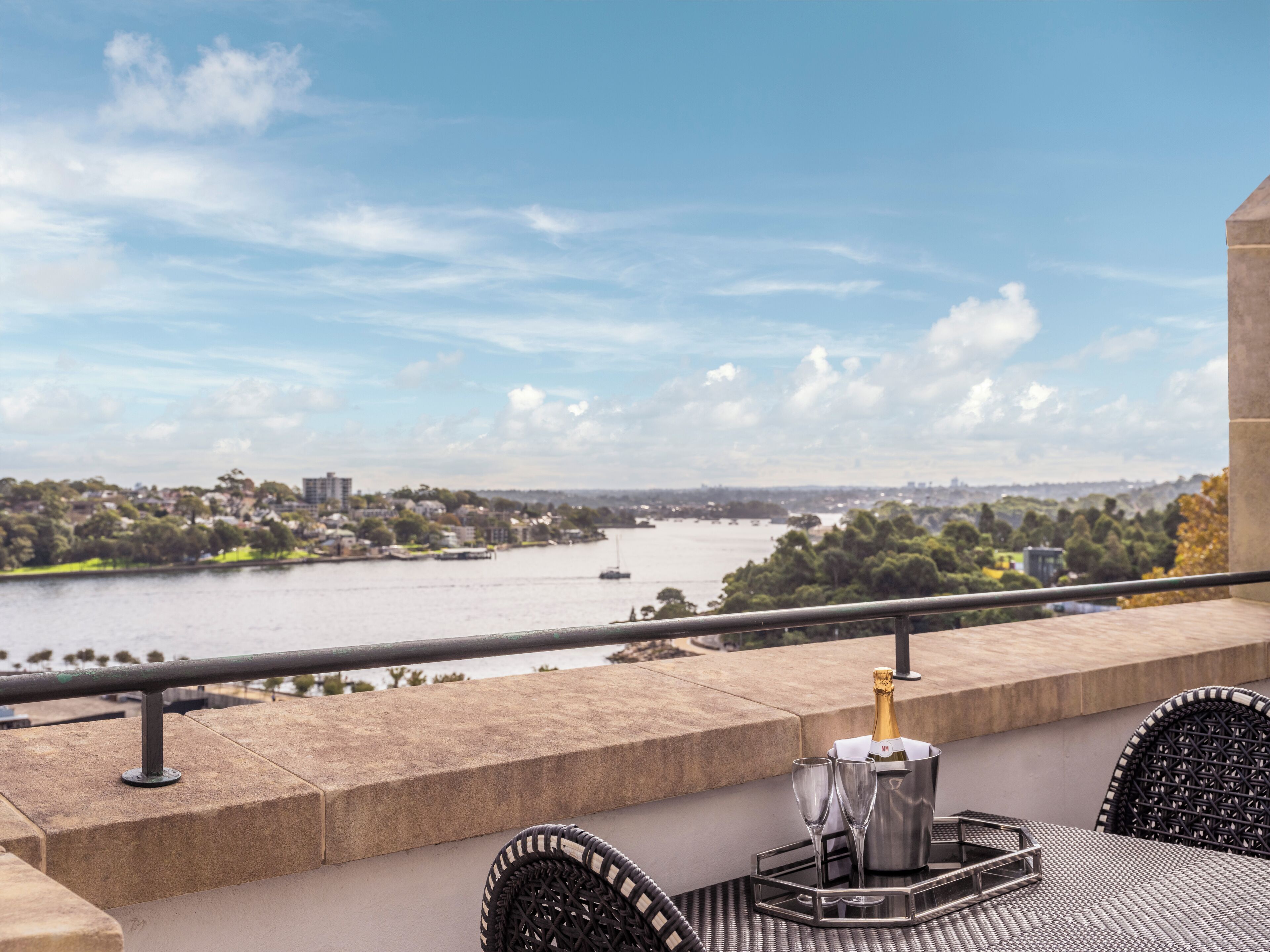 A balcony with a view of a river, a bottle of champagne, and two glasses on a tray.