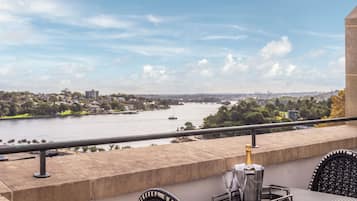 A balcony with a view of a river, a bottle of champagne, and two glasses on a tray.