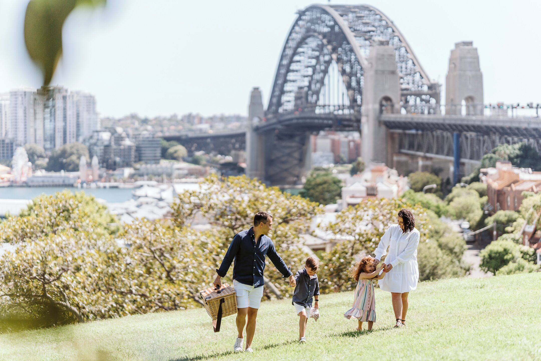 A family walking on a grassy hill with a cityscape and a bridge in the background.