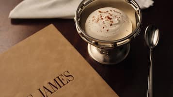 Un postre en un vaso de metal con una cuchara al lado, sobre una mesa con una servilleta y una bolsa de papel marrón con el texto 'THE JAMES'.