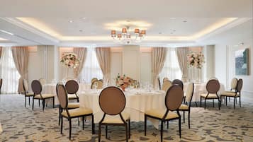 Un comedor elegante con mesas redondas, sillas y una araña.