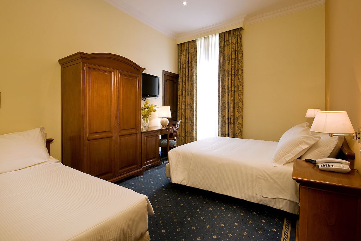 A hotel room with two beds, a wooden wardrobe, a desk with a lamp, and a telephone.