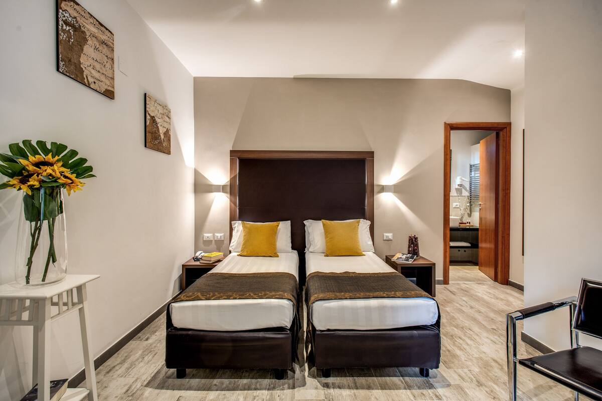 A hotel room with two beds, a small table with a vase of flowers, and a chair.