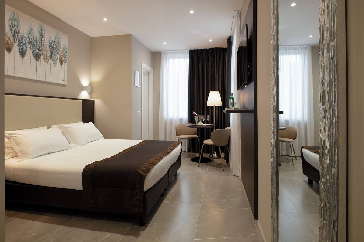 A hotel room with a large bed, a desk with chairs, a TV, and a painting on the wall.