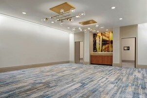 A spacious room with a patterned carpet, recessed ceiling lights, and a large artwork on the wall.