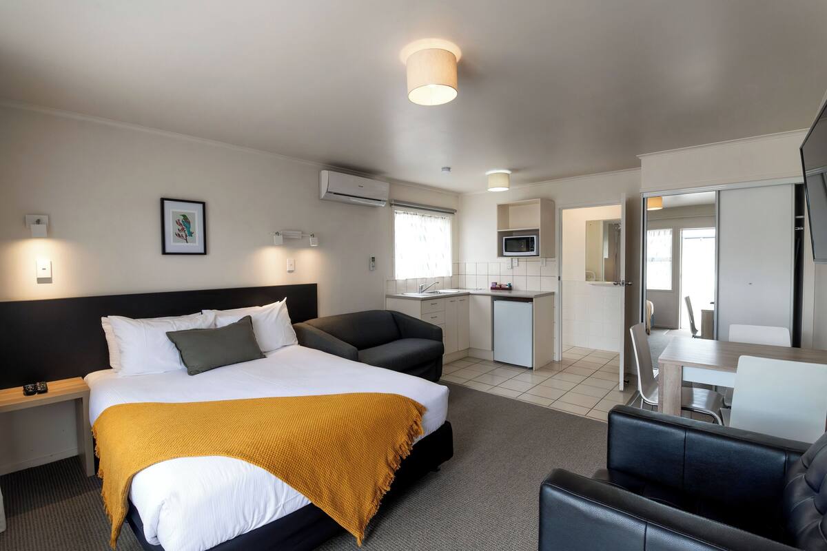 Habitación de hotel con cama, sofá, escritorio, microondas y baño visible a través de una puerta abierta.