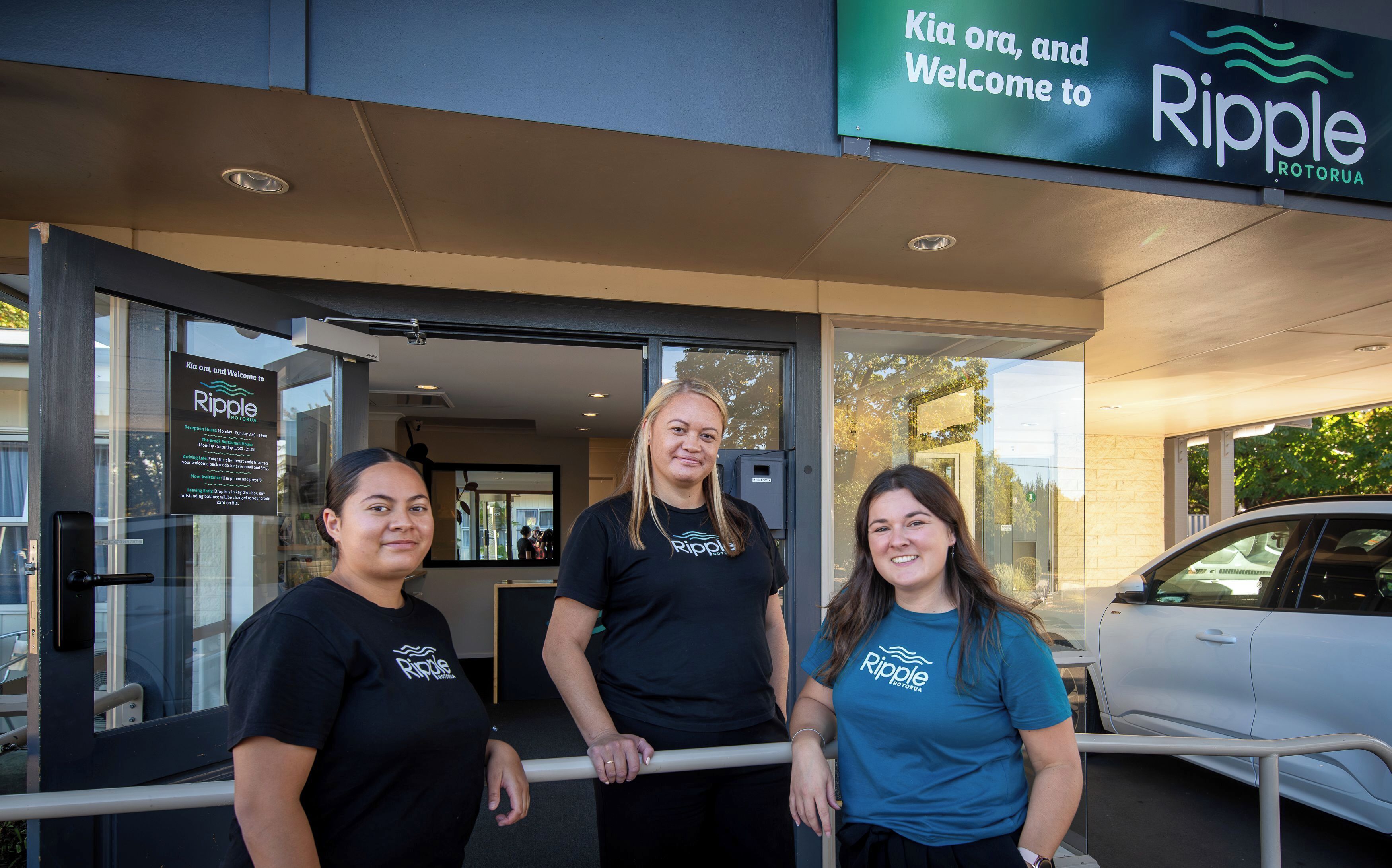 Tres personas de pie frente a un edificio con un letrero que dice 'Kia ora, and Welcome to Ripple Rotorua'.
