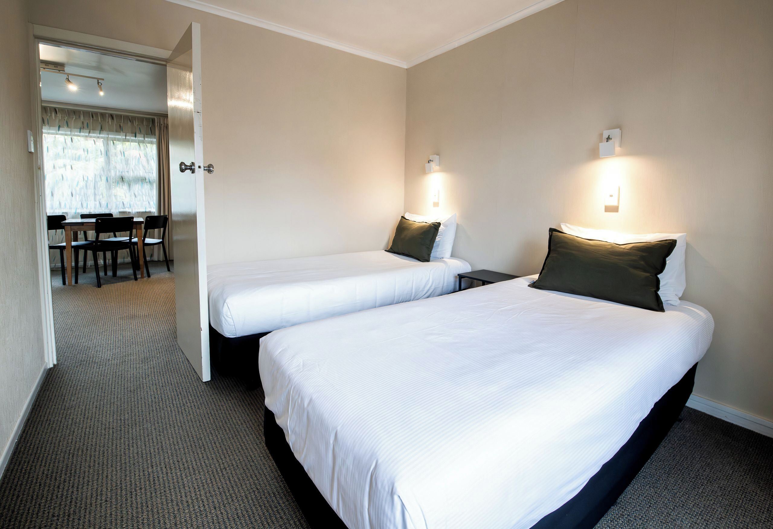 A hotel room with two single beds, a small table, and a chair.