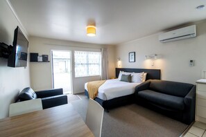 A modern hotel room with a bed, a sofa, a desk, and a TV.